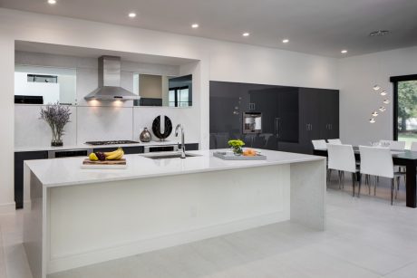 Modern, minimalist kitchen with sleek white countertops, black cabinetry, and a dining area in the background.