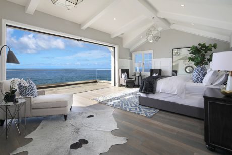 Elegant coastal-inspired bedroom with panoramic ocean view, vaulted ceiling, and modern furnishings.