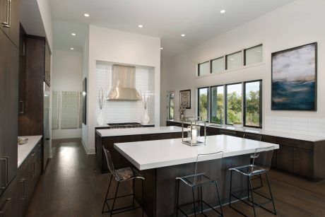 A modern kitchen with sleek cabinetry, minimalist lighting, and large windows overlooking greenery.