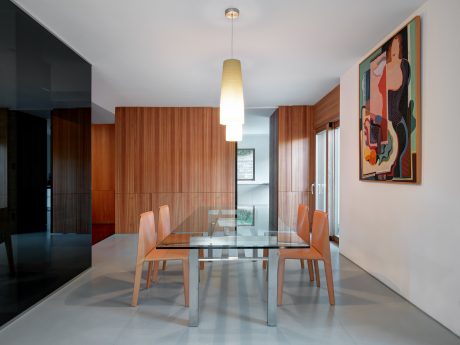 Sleek, modern dining area with glass table, wooden walls, and contemporary artwork.