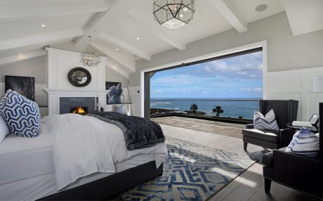 Luxurious bedroom with vaulted ceiling, fireplace, and panoramic ocean view through large windows.