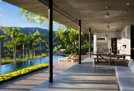 Expansive modern interior with floor-to-ceiling windows overlooking a tropical pool surrounded by lush greenery.