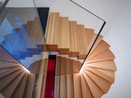 Spiral staircase with layered wooden steps, reflective glass panels, and lighting.