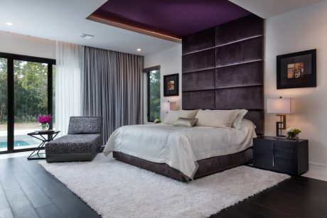Luxurious bedroom with plush purple headboard, chaise lounge, and panoramic window views.