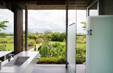 Expansive glass doors frame a lush, tropical garden landscape. Modern, minimalist interior features.