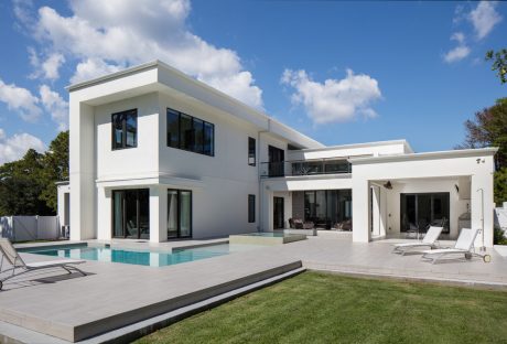 Modern, minimalist two-story home with a rectangular pool, outdoor seating, and lush landscaping.