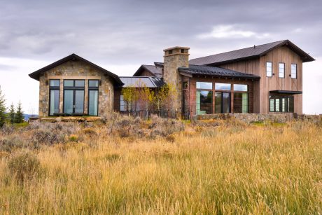 A rustic mountain home with stone accents, large windows, and a spacious porch.