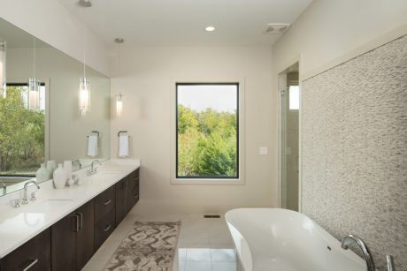 Spacious modern bathroom with large window, double vanity, and sleek tiled walls.