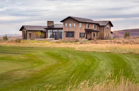 A large, rustic-style vacation home with stone, wood, and glass elements set against a scenic landscape.