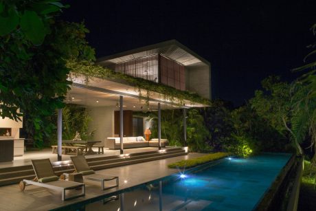 Modern tropical villa with sleek concrete design, illuminated pool, and lush foliage.