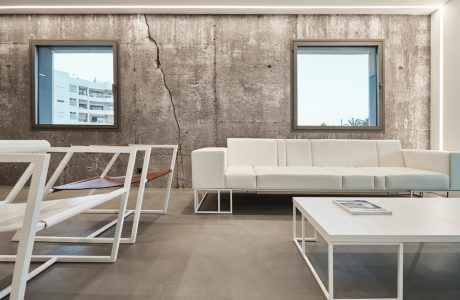 Minimalist living room with concrete walls, white furniture, and framed windows.