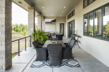 Spacious covered patio with stone columns, wicker furniture, and a decorative floor rug.