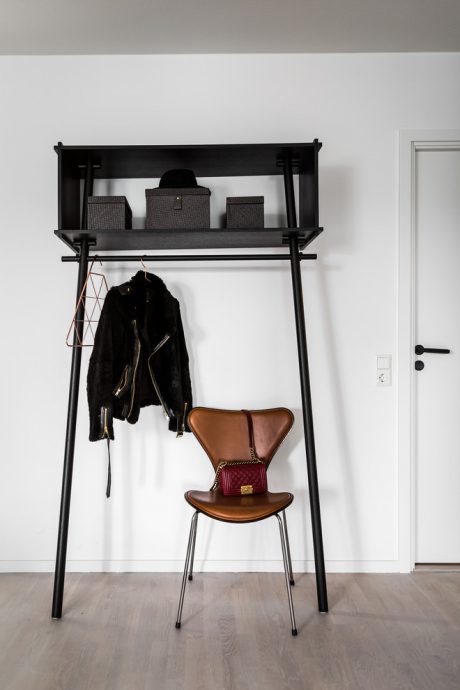 Minimalist black metal rack with shelves, coat hooks, and a leather chair against a white wall.