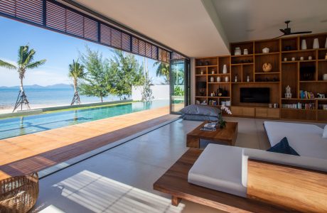Airy, open-concept living space with floor-to-ceiling windows, infinity pool, and modern, wooden furnishings.