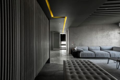 Dark, modern interior with vertical striped walls, concrete floor, and a gray tufted sofa.