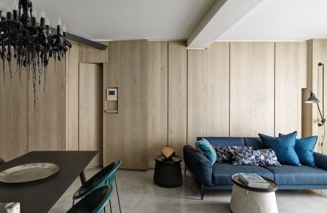 Sleek, modern living space with wooden paneling, dark sofa, and statement chandelier.