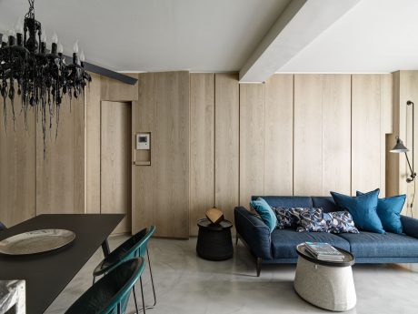 Sleek, modern living space with wooden paneling, dark sofa, and statement chandelier.