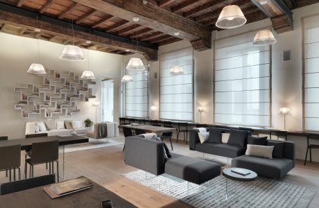 A modern, open-concept living room with exposed wooden beams, modular sofas, and pendant lights.