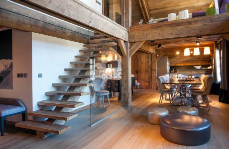 Rustic wooden cabin interior with open staircase, dining area, and plush furnishings.