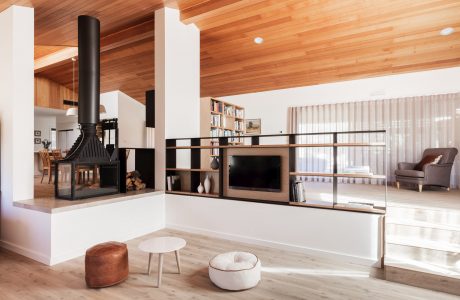 Modern open-plan living room with wooden beamed ceiling, fireplace, and built-in shelving.