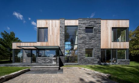 A modern, minimalist home featuring a mix of wooden and stone exterior, large windows, and a patio.