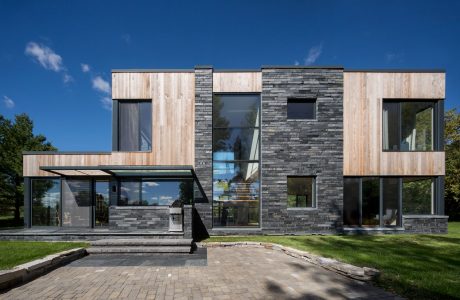 A modern, minimalist home featuring a mix of wooden and stone exterior, large windows, and a patio.