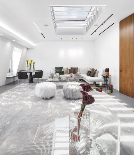 A sleek, modern living room with a minimalist glass and metal chandelier, plush seating, and decorative accents.