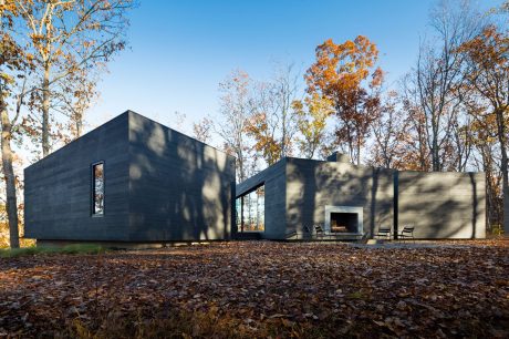 A modern black minimalist home nestled in a forest with an inviting outdoor fireplace.