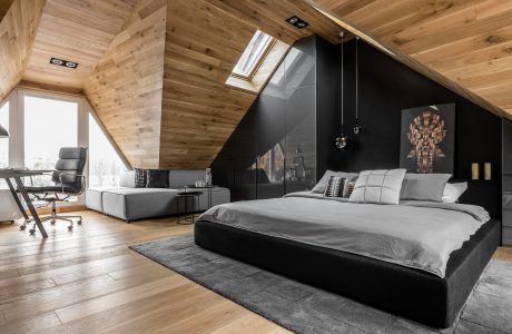 Cozy attic bedroom with wooden walls, slanted ceiling, and modern black furniture.