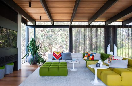 A modern, open-plan living space featuring wooden beams, floor-to-ceiling windows, and vibrant furniture.