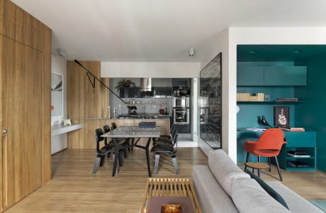 An open-concept space with a modern, minimalist kitchen and dining area, accented by vibrant teal and warm wooden tones.