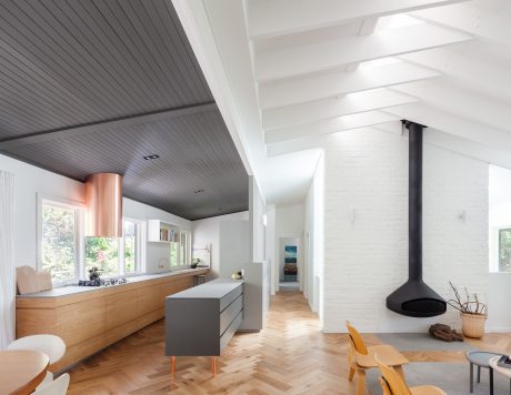 Bright, open-concept living space featuring modern kitchen, wood-beamed ceiling, and freestanding fireplace.