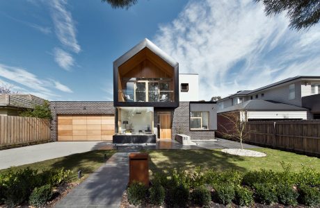 Modern two-story home with wooden and brick exterior, large windows, and landscaped yard.