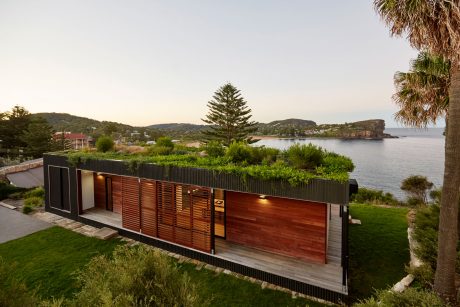 Modern waterfront home with wooden slatted facade and extensive greenery on the roof.