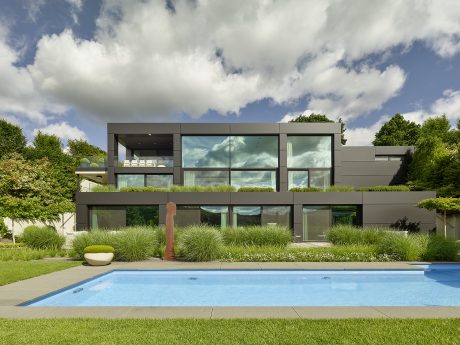 Modern, minimalist residence with glass façade, outdoor pool, and lush landscaping.