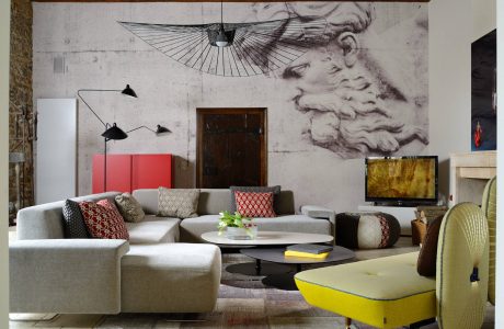 A modern, eclectic living room with a large mural, curved sofa, and vibrant accents.