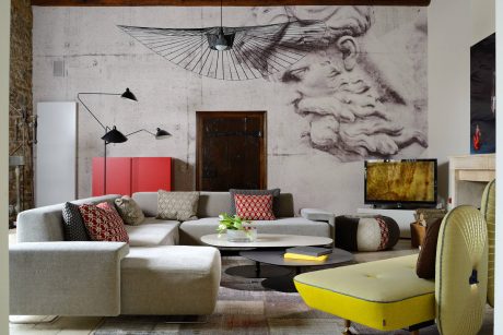 A modern, eclectic living room with a large mural, curved sofa, and vibrant accents.