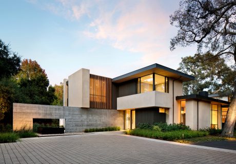 Modern, multi-level home with striking concrete and wood exterior, large windows, and lush landscaping.