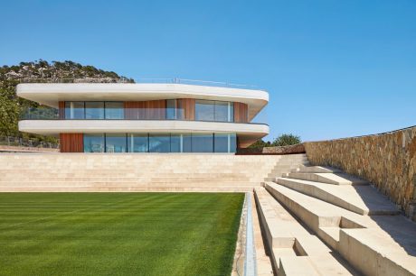 Modern, multi-level residential building with glass walls, wood accents, and cascading stone steps leading to lush lawn.