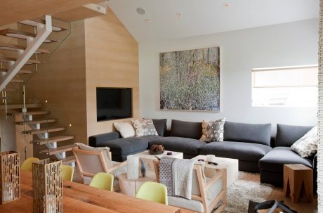 Spacious, modern living room with glass staircase, plush gray sofa, and wooden accents.