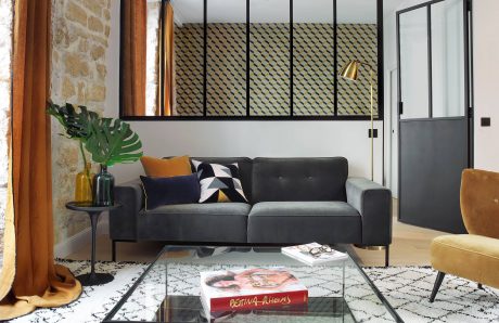 A modern, stylish living room featuring a gray sofa, patterned rug, and brass accents.