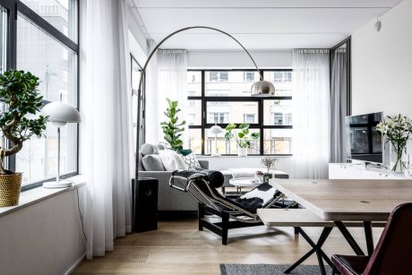 Elegant modern living room with arched floor lamp, wood dining table, and potted plants.