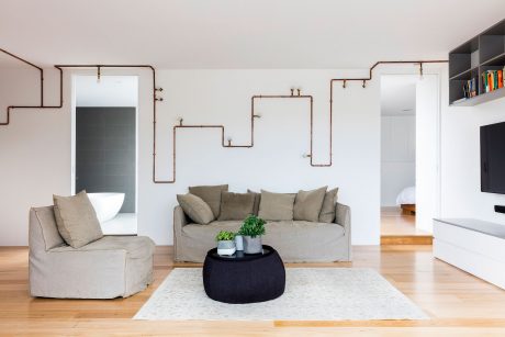 Minimalist living room with exposed copper plumbing as decorative wall feature.