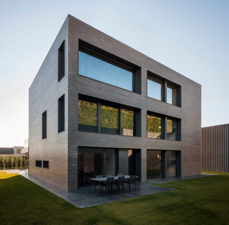 A modern, minimalist house with sleek, dark wooden facade, large windows, and an outdoor patio.