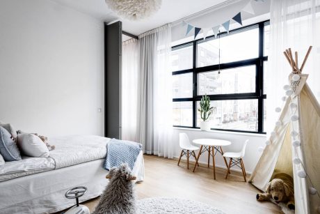 A bright, modern children's bedroom with large windows, soft furnishings, and an accent light fixture.