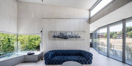 Minimalist concrete interior with large blue tufted sofa and abstract artwork.