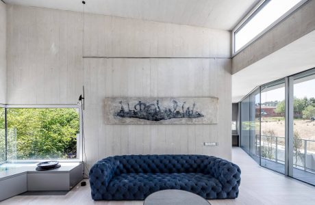 Minimalist concrete interior with large blue tufted sofa and abstract artwork.