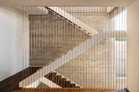 A modern, minimalist staircase with a grid-like cable railing design and exposed brick wall.