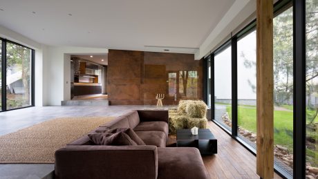 Spacious modern living room with wooden beams, large windows, and plush brown sofa.