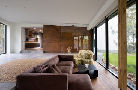 Spacious modern living room with wooden beams, large windows, and plush brown sofa.